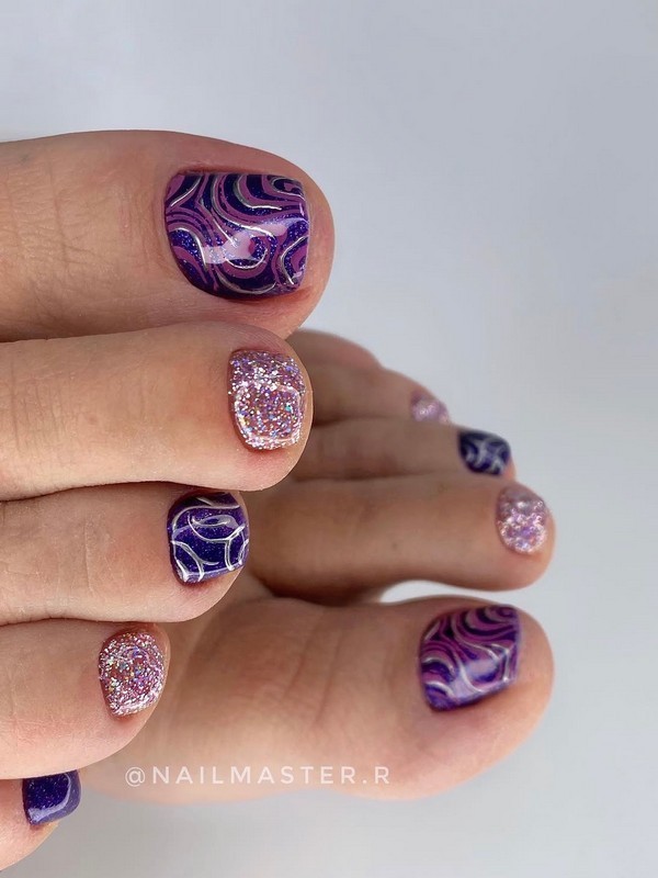 Purple galaxy pedicure features a vibrant design with glitter and abstract swirls, creating a cosmic effect. Perfect for a bold and eye-catching look.